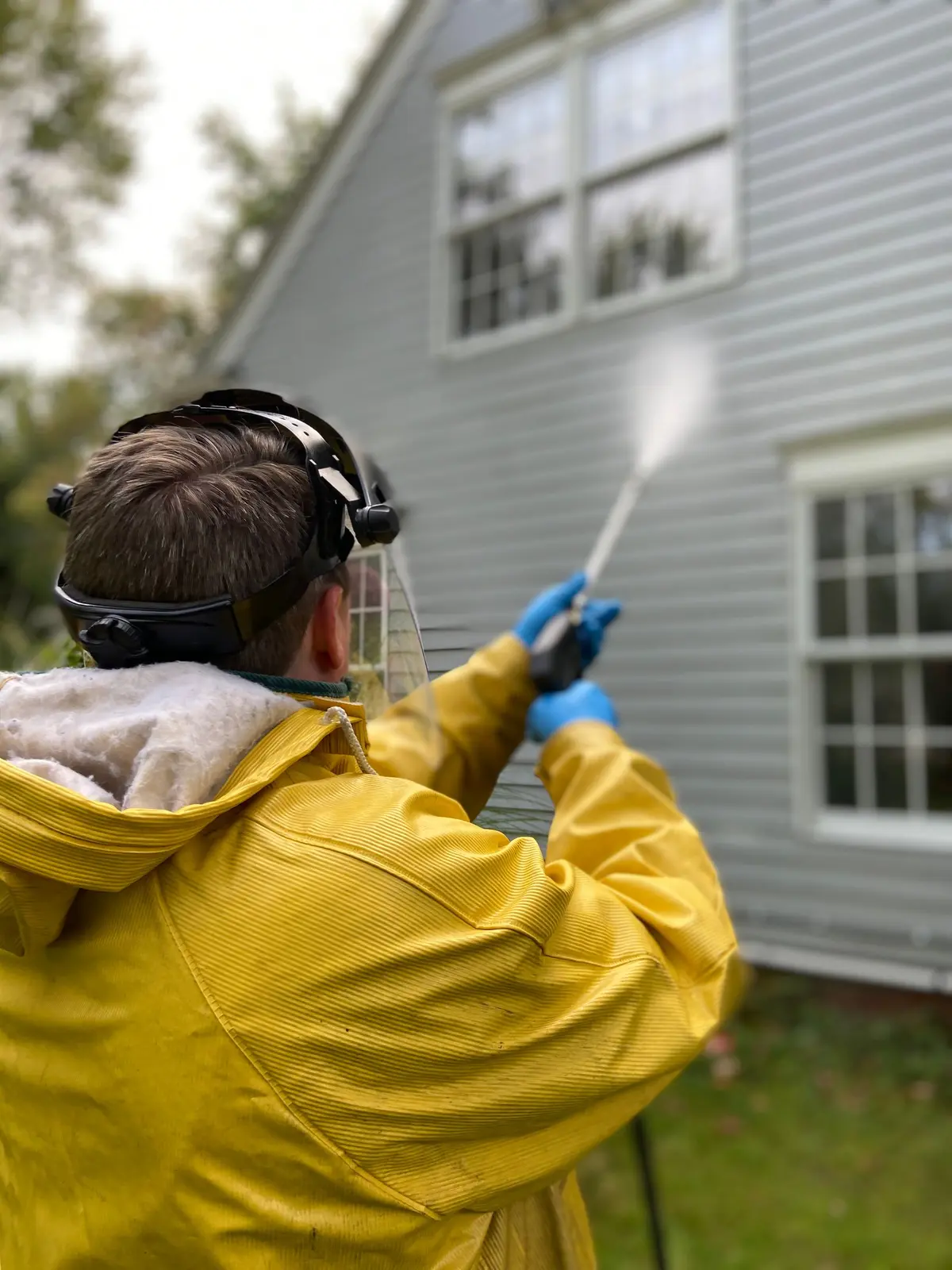 Pressure washing the grey siding of a two-story home